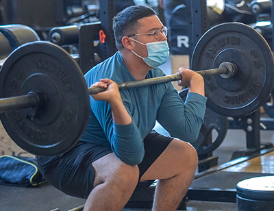 student in mask lifting weight
