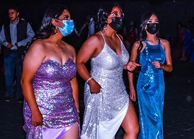 three girls in prom dresses and masks on dance floor