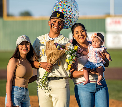 smiling baseball player with baby mom and wife